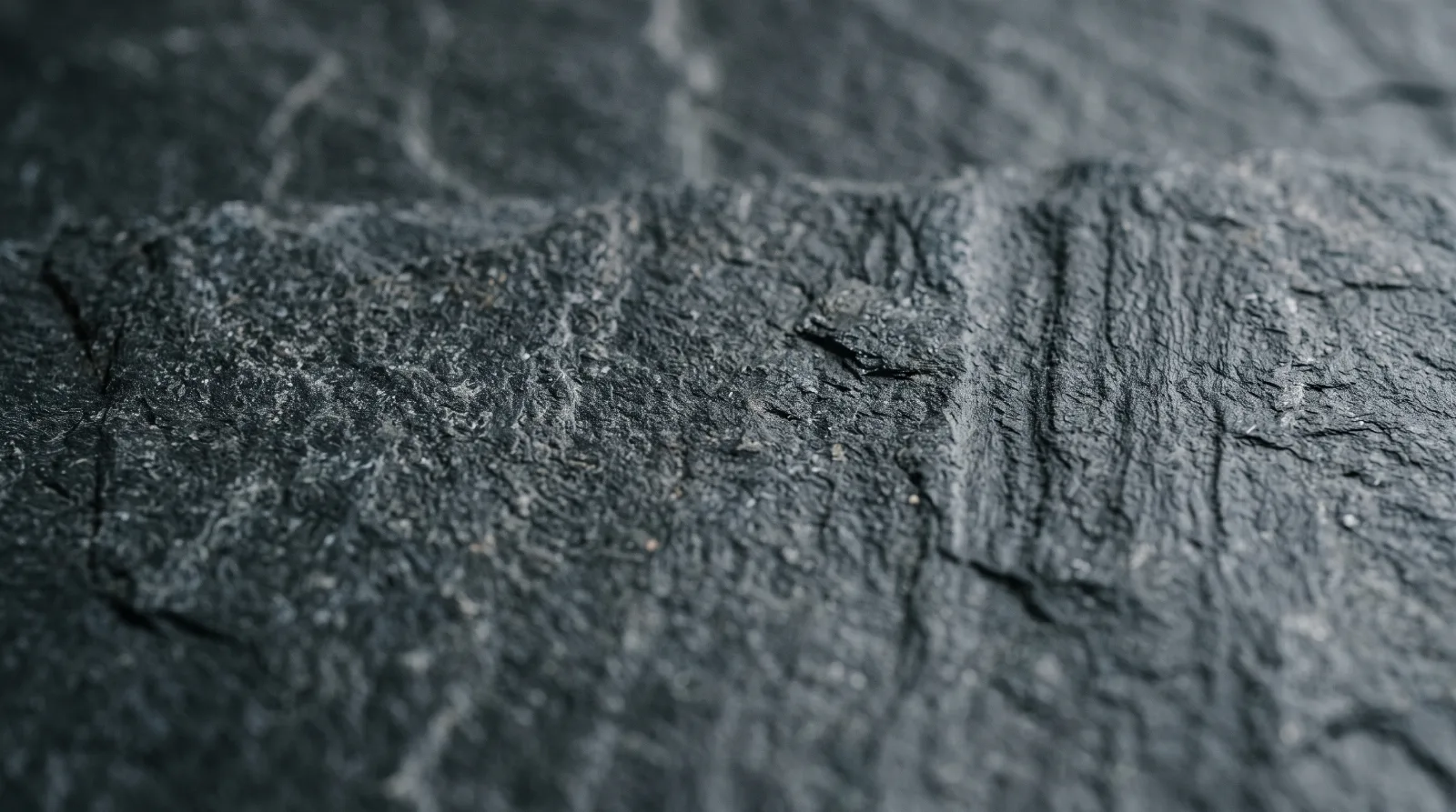 Detailaufnahme einer matten, dunklen Natursteintextur im Streiflicht als Materialbeispiel für ein Kolumbarium.